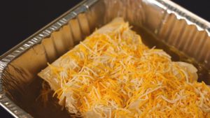 Cheesy enchiladas in a metal container.