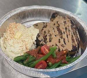 A metal container with mashed potatoes and green beans.