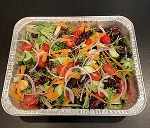 A salad in a foil container on a table.